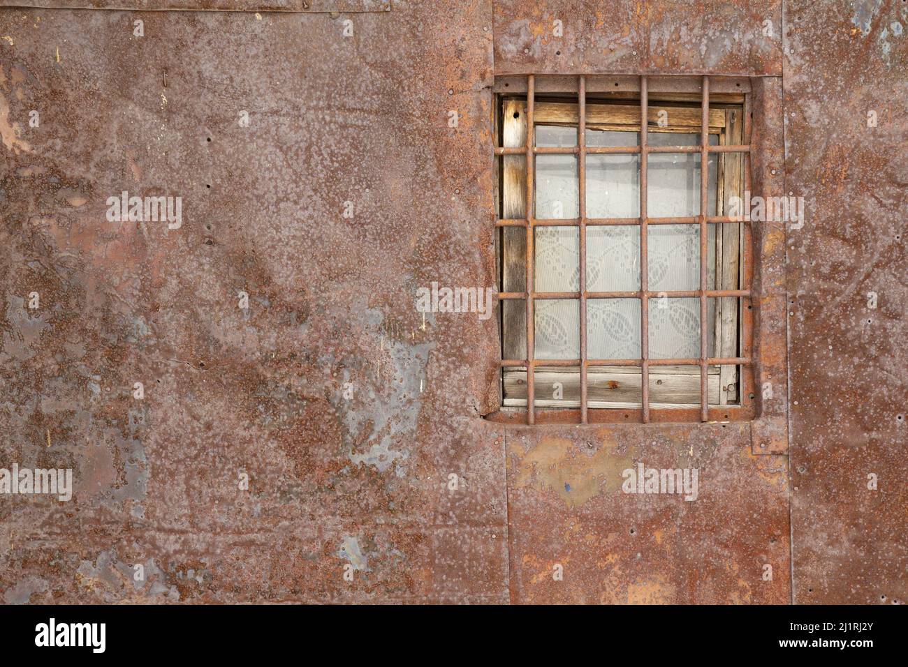 Autentico sfondo marrone naturale con tinte rosse. Una prigione di metallo sbarre sulla finestra di una vecchia casa che assomiglia ad una prigione rivestita di metallo shee Foto Stock