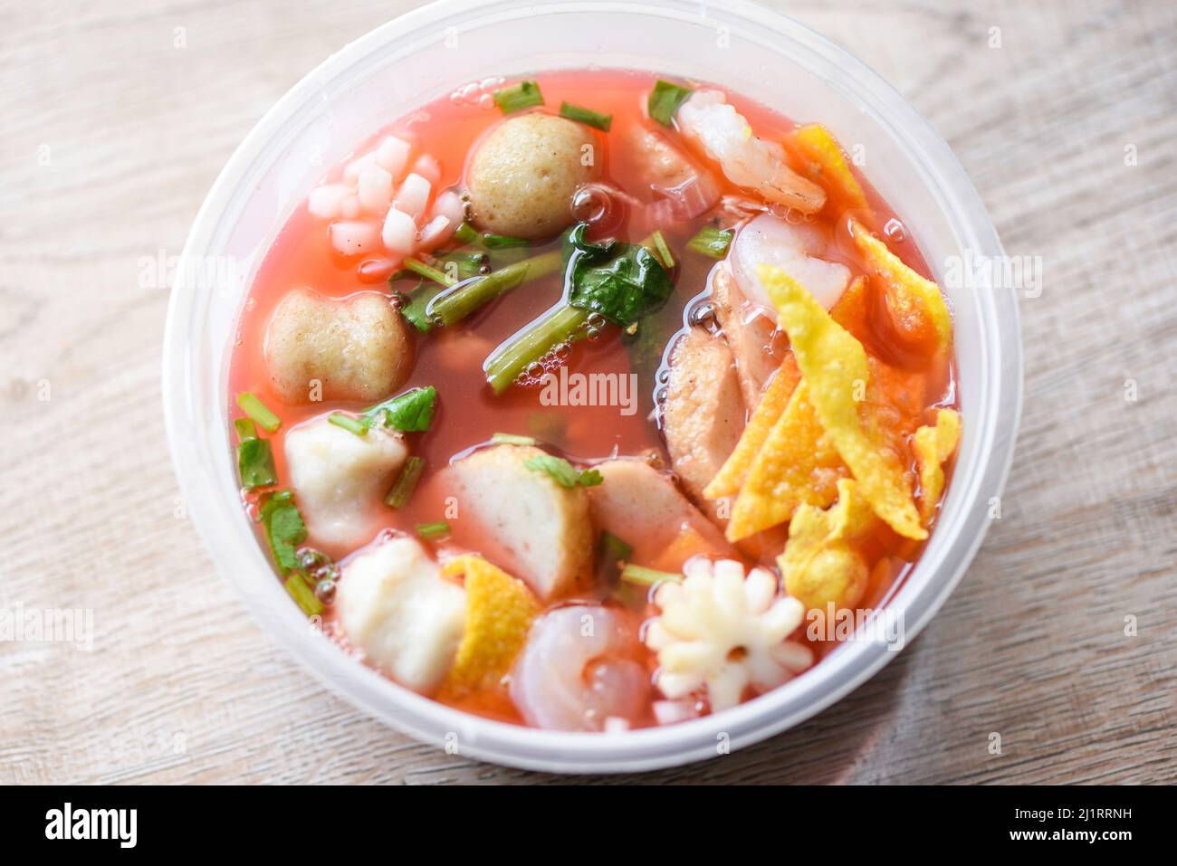 Zuppa rossa palle di maiale croccanti wontons con pesce calamari gamberi e palle di pesce verdure in zuppa ciotola plastica su tavolo di legno, vista dall'alto Thai e C. Foto Stock