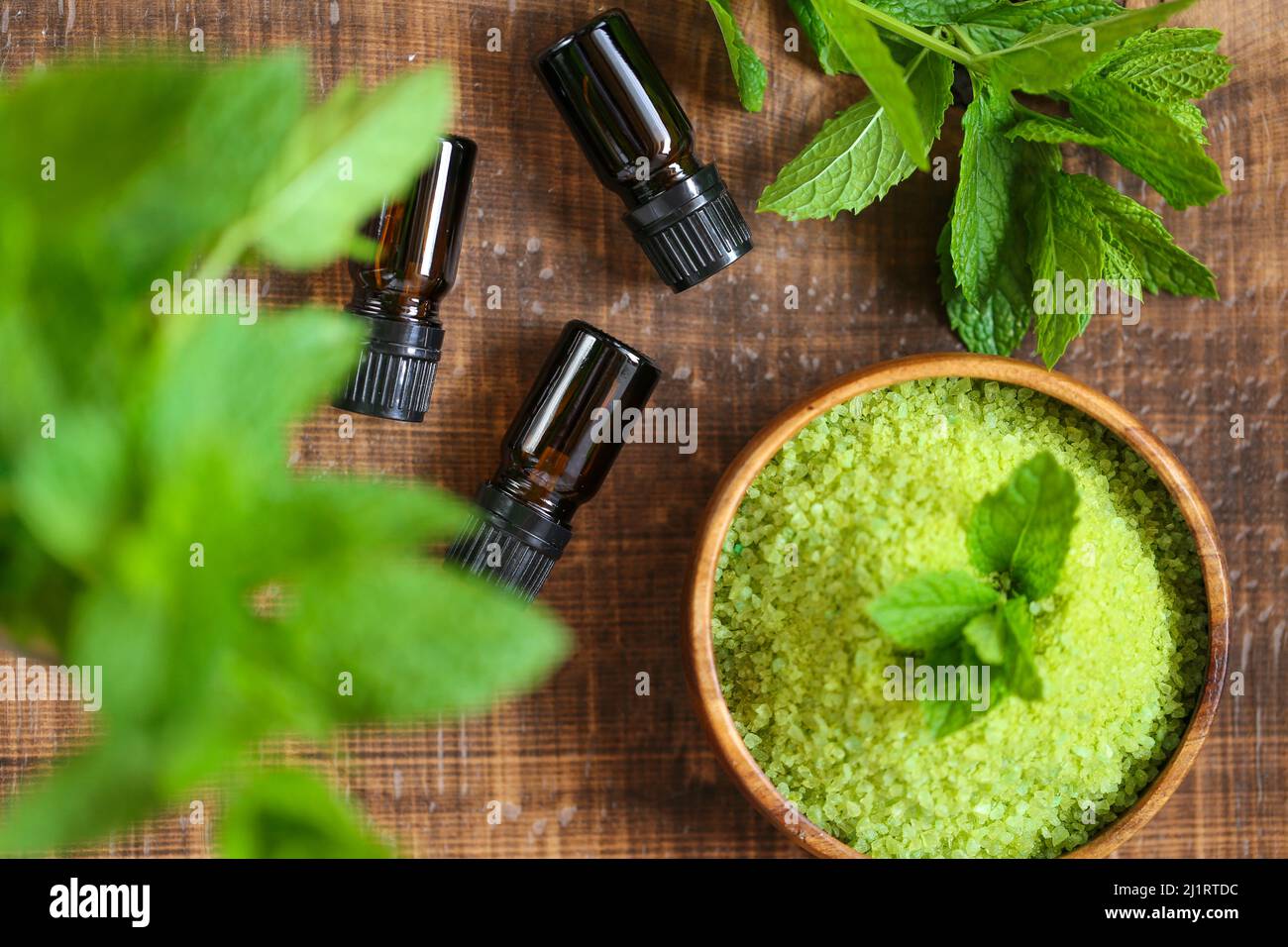 Bottiglia di olio essenziale di menta piperita.vetro, menta piperita fresca e sale marino verde con estratto di menta su sfondo legno di tavola. Foto Stock