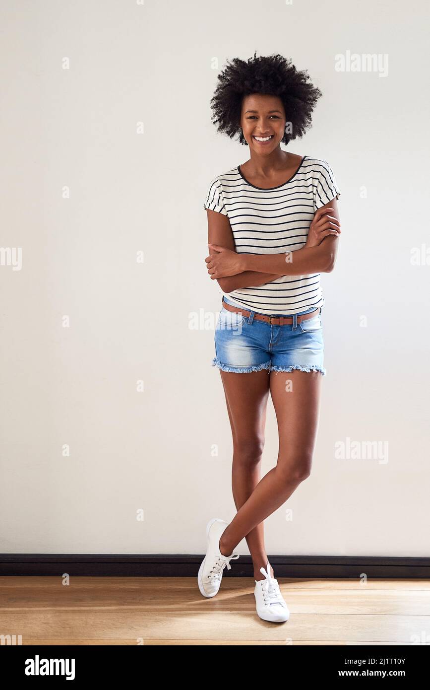 I suoi shorts stagione di nuovo. Ritratto di una giovane donna attraente e felice che indossa un pullover a righe e pantaloncini in denim in interni. Foto Stock