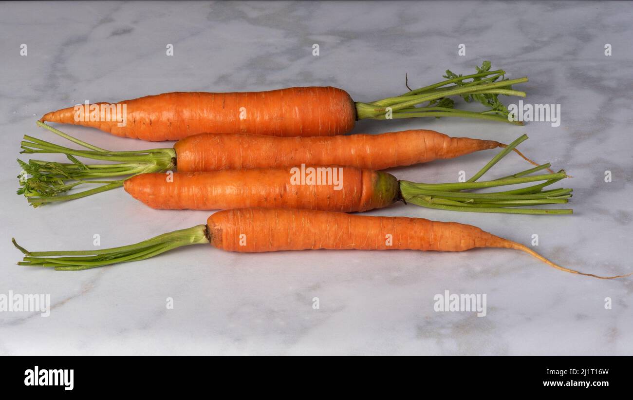 Vista angolare delle carote organiche in parallelo su sfondo di marmo bianco, con copyspace - concetto di cibo sano Foto Stock