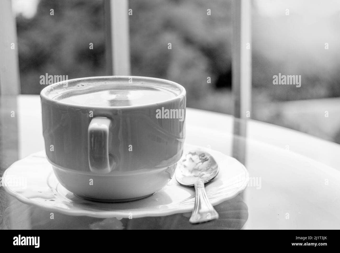 Caffè in una tazza su un tavolo di vetro, vista laterale, colazione sul balcone, foto in bianco e nero. Foto Stock