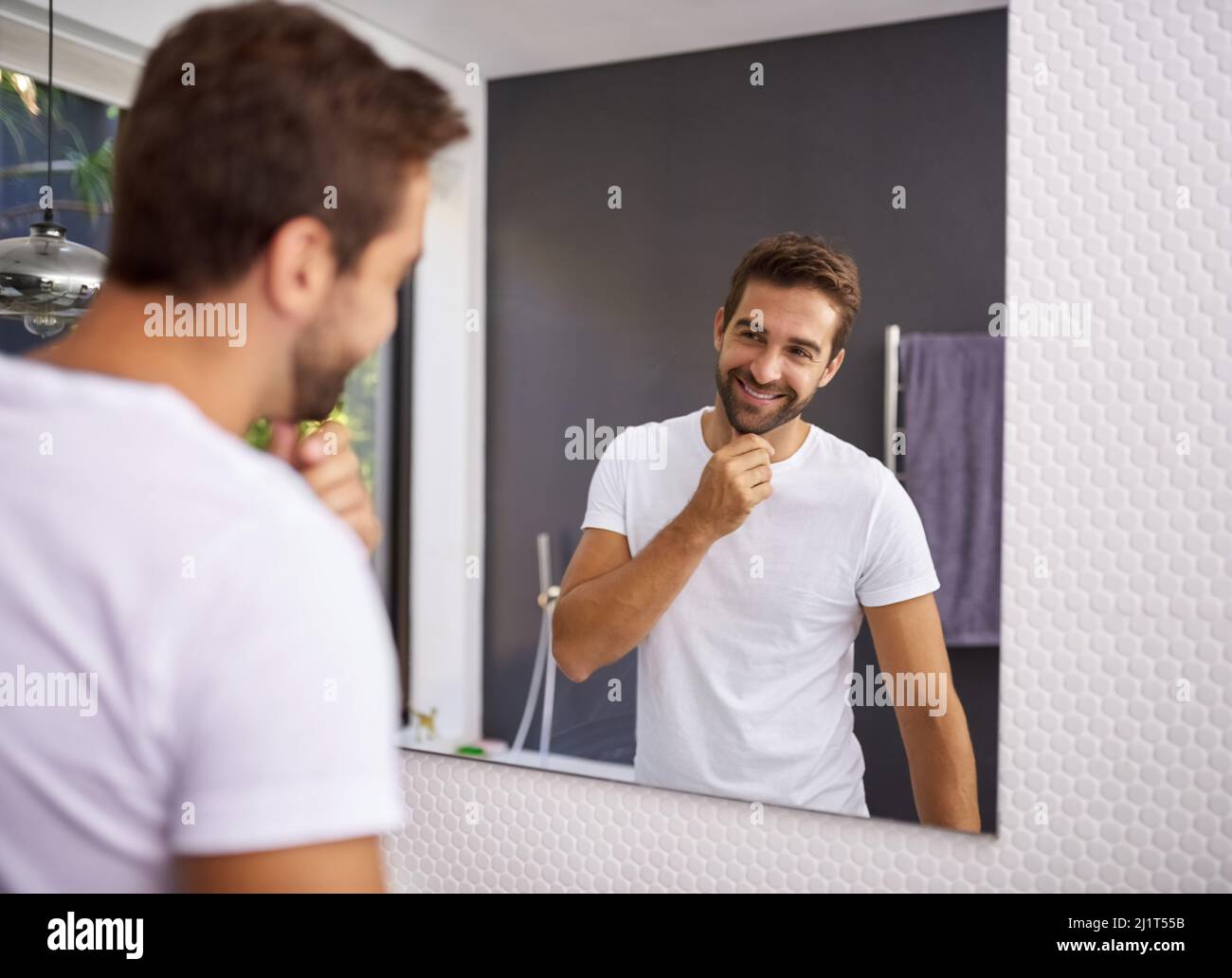 Comunque, mi aspetto bene con una barba. Scatto corto di un bell'uomo che si guarda nello specchio mentre tocca la barba a casa. Foto Stock