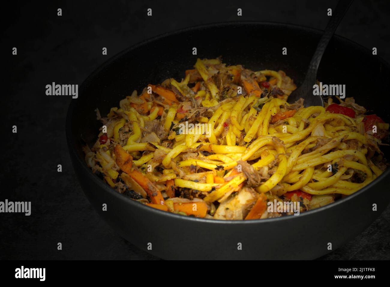 Anatra grattugiata mescolare friggere con spezie e verdure in un recipiente nero. Su sfondo di pietra Foto Stock