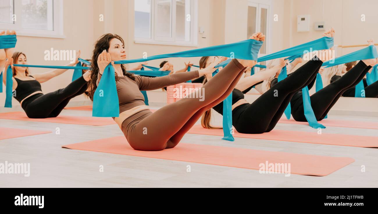Gruppo di donne di mezza età con istruttore di fitness in leggings sportivi e top, facendo Pilates con il nastro di gomma sul tappeto yoga vicino al Foto Stock