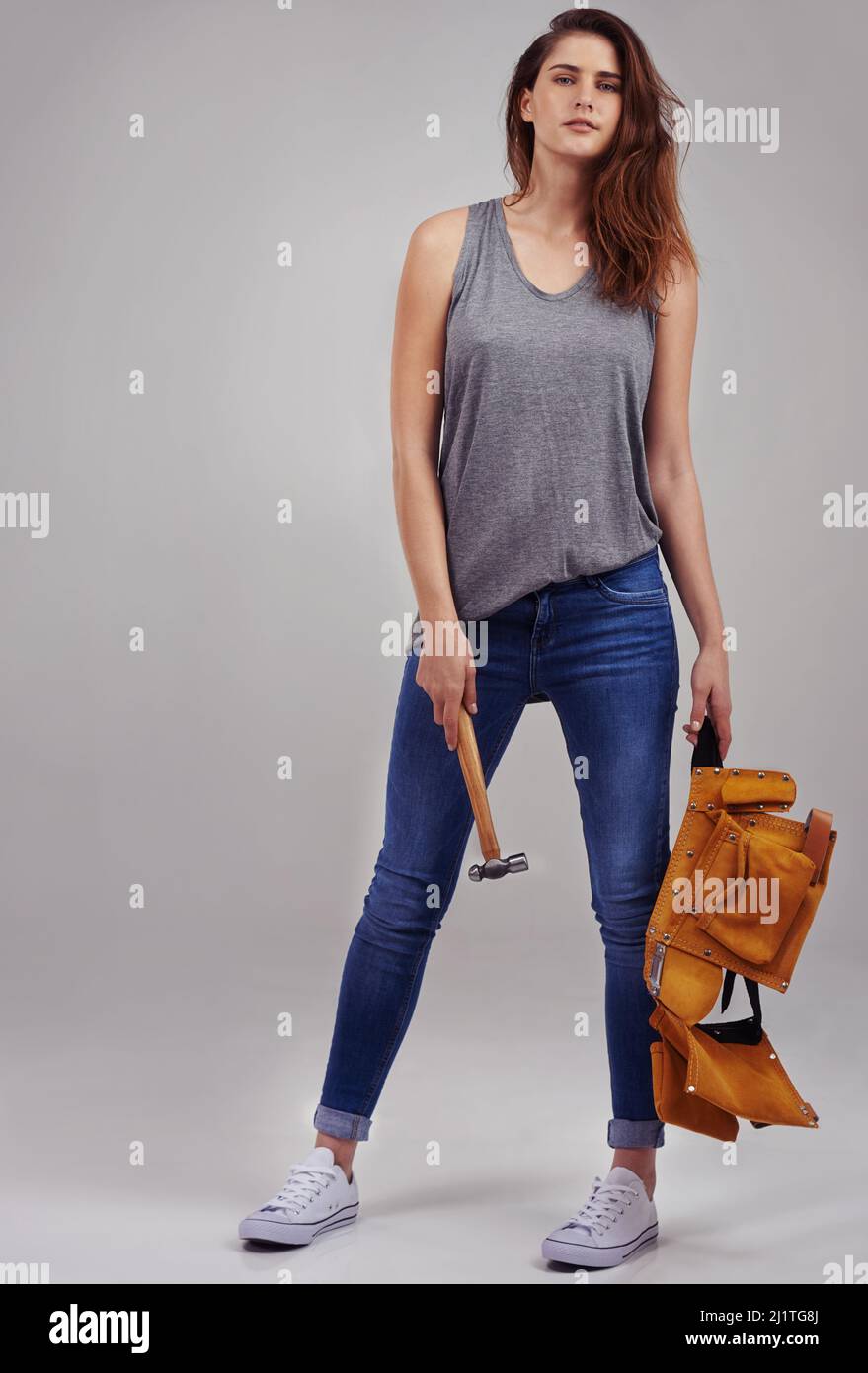 Posso risolvere qualsiasi problema. Ritratto completo in studio di una giovane donna vestita casualmente che tiene un martello e una cintura portautensili. Foto Stock