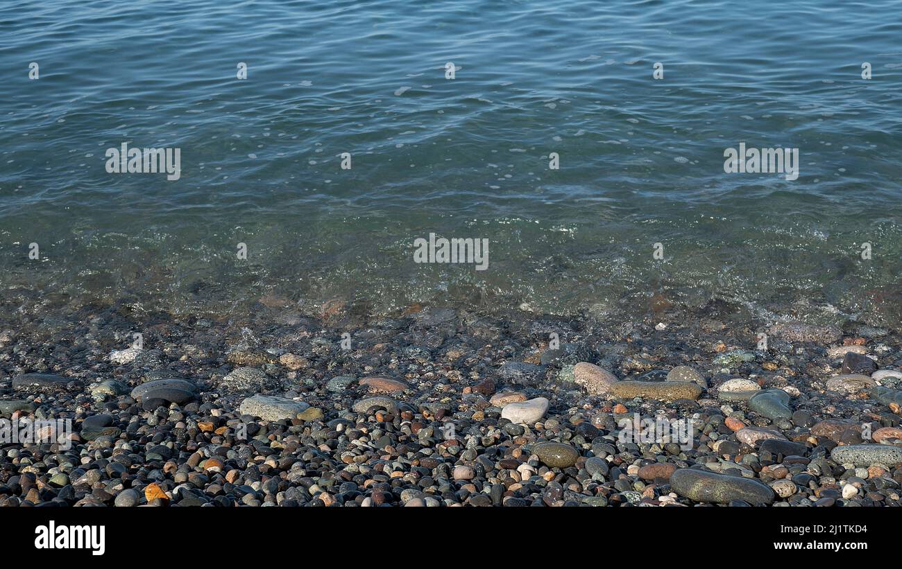 Primo piano sul mare. Ciottoli multicolore sul bordo dell'acqua. Mare trasparente e pulito. Giornata di sole in vacanza Foto Stock