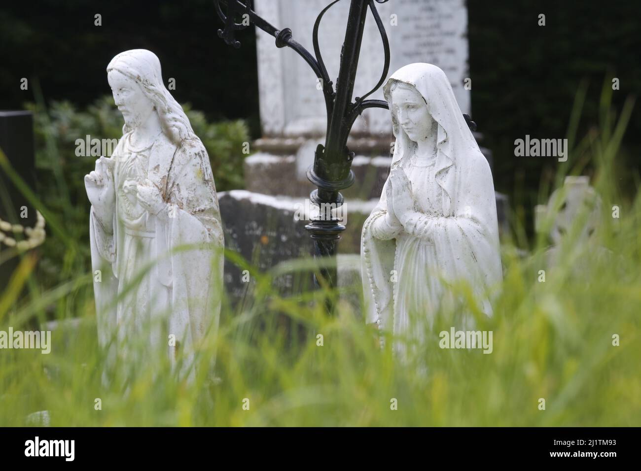 Statue religiose in un cimitero in Irlanda tra altri simboli cattolici, tra cui una croce celtica. Foto Stock