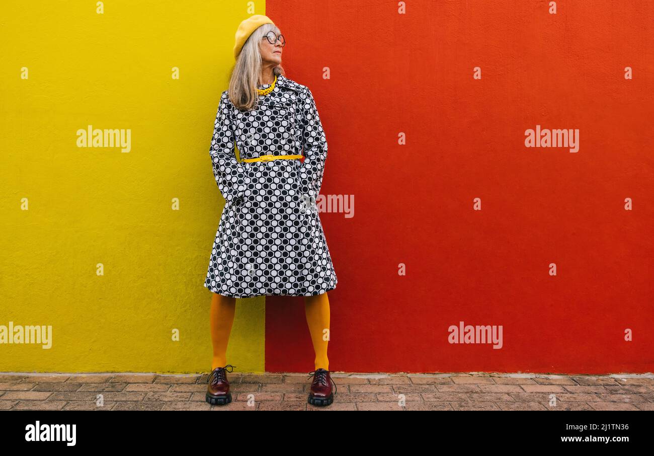 Donna matura che guarda via pensierosamente mentre si alza su uno sfondo colorato. Donna anziana pensiva che riflette sulle memorie del passato. Senior Foto Stock