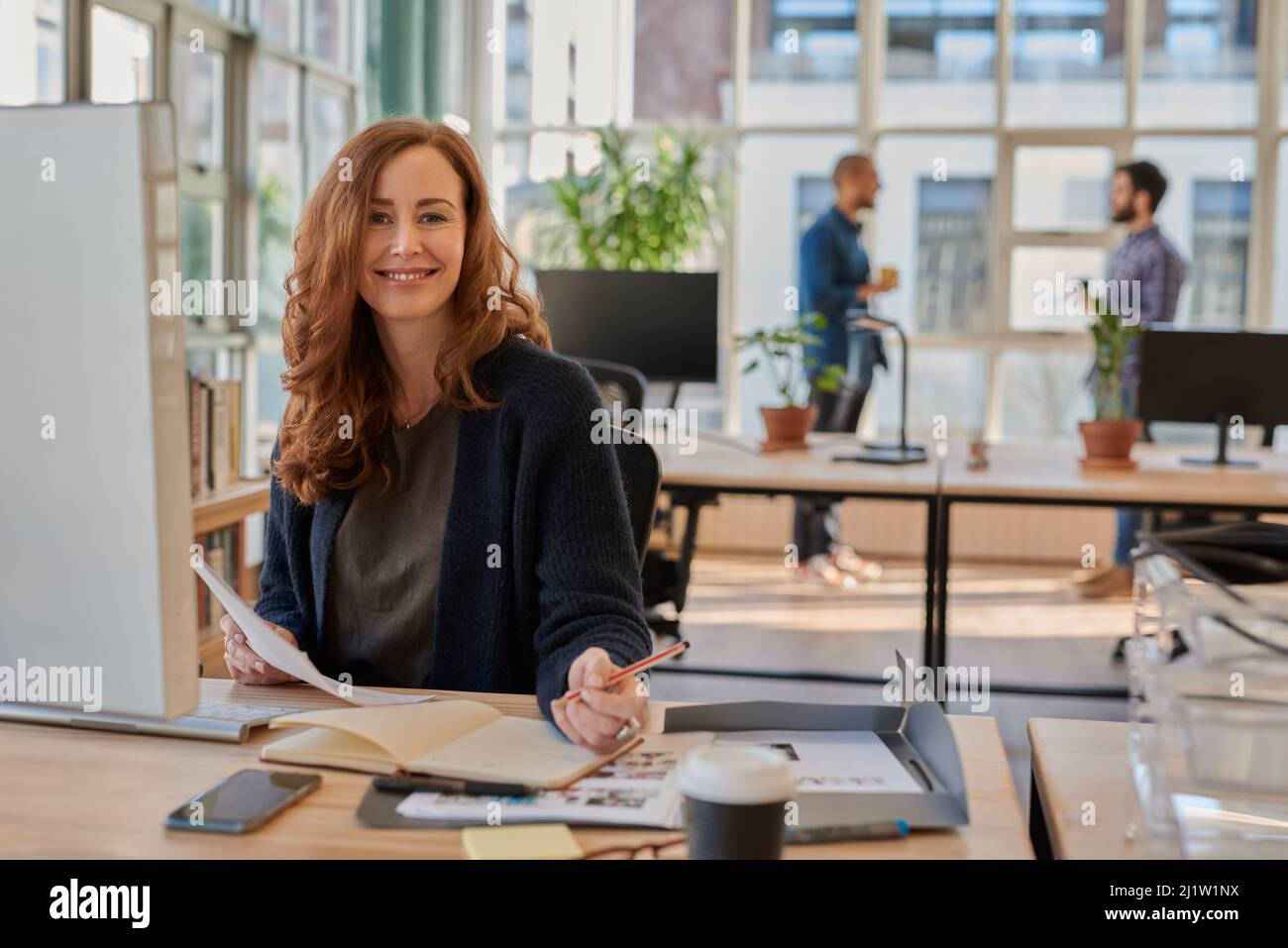 Donna d'affari sorridente che lavora in ufficio con colleghi in background Foto Stock