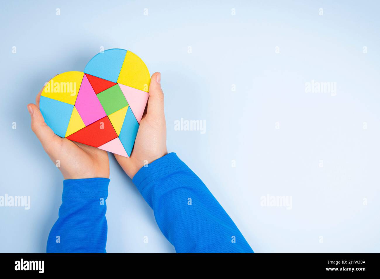 Le mani del bambino tengono il cuore colorato del puzzle su sfondo azzurro chiaro. Concetto di giornata di consapevolezza autismo mondiale Foto Stock