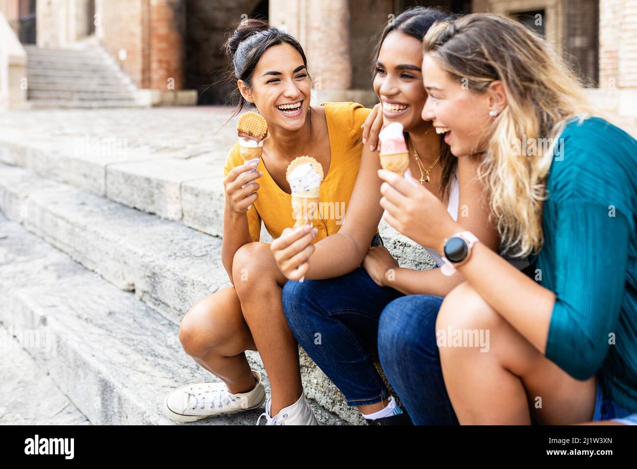 Felice donne multirazziale mangiare gelato all'aperto mentre si siede alle scale Foto Stock