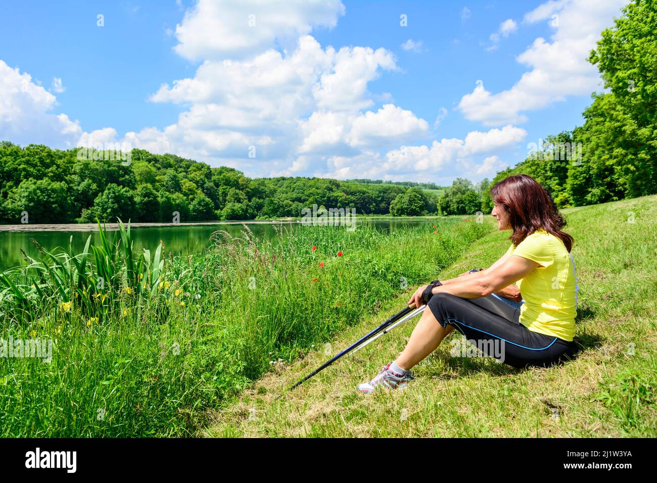 Due donne sportive che fanno una pausa durante un'esercitazione nordic walking vicino un piccolo stagno Foto Stock