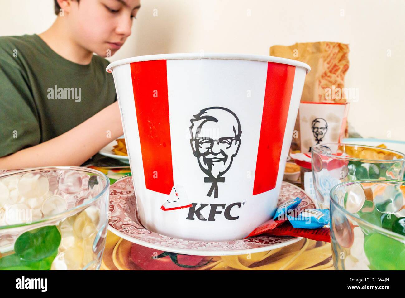 Un ragazzo sedette al tavolo della sala da pranzo e gustatevi un pasto insieme con pollo fritto acquistato da KFC. Foto Stock