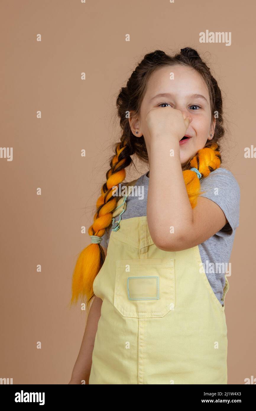 Caucasica che brilla femmina con trecce gialle kanekalon, guardando la  macchina fotografica sorridendo e toccando il naso con le dita in tuta  gialla e t grigio Foto stock - Alamy