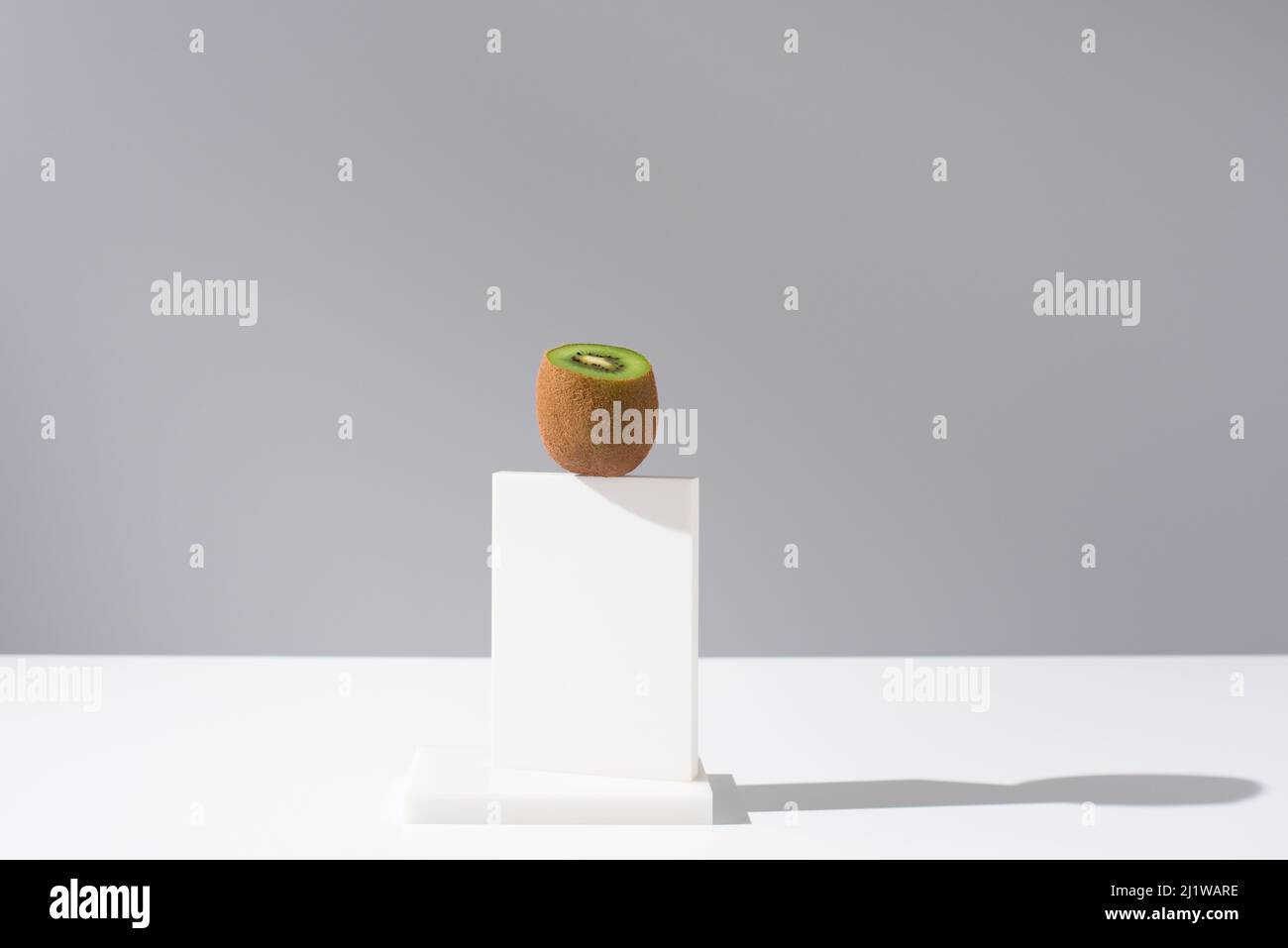 Tagliare il kiwi fresco senza buccia posto su un piedistallo bianco sul tavolo su sfondo grigio in studio chiaro Foto Stock