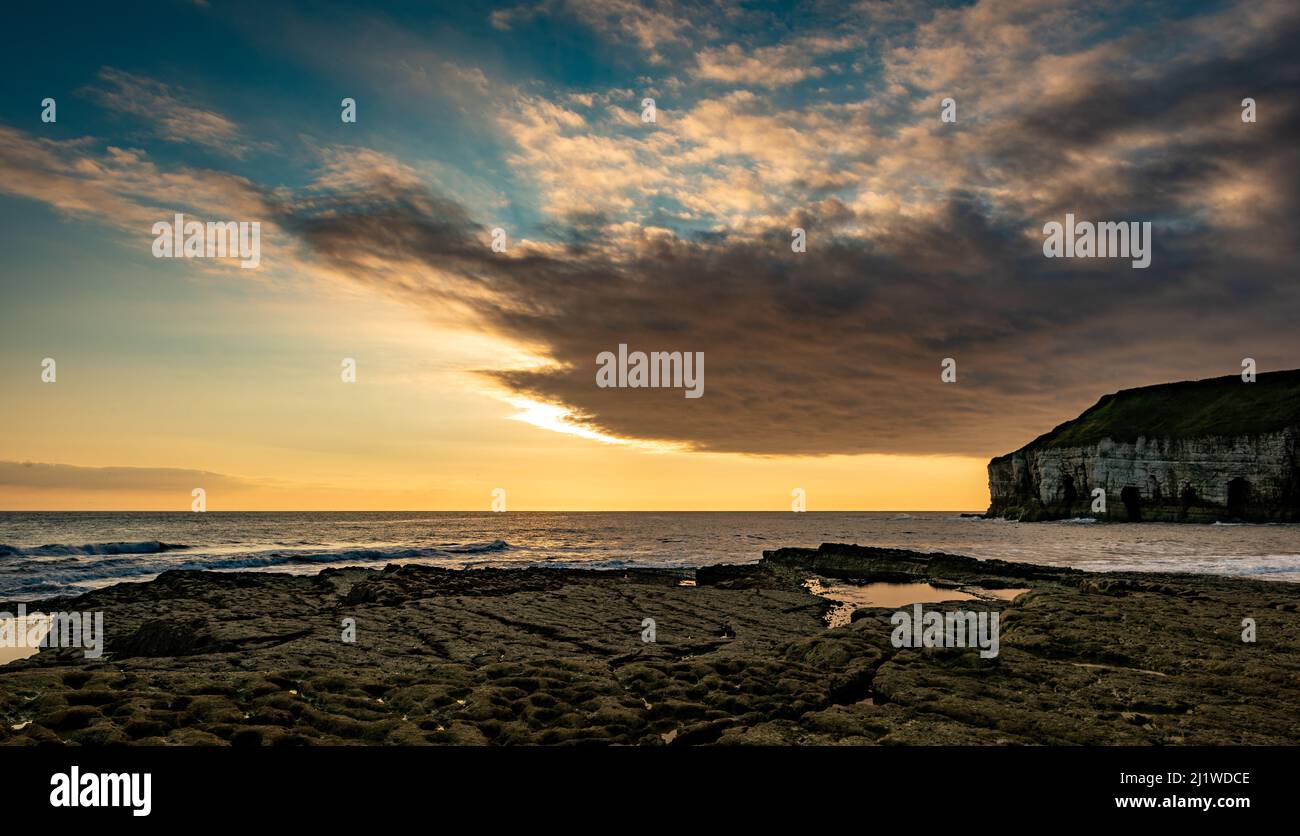 Una grande nuvola spessa si muove dentro e copre il sole che sorge. Thornwick Bay, costa dello Yorkshire, Regno Unito Foto Stock