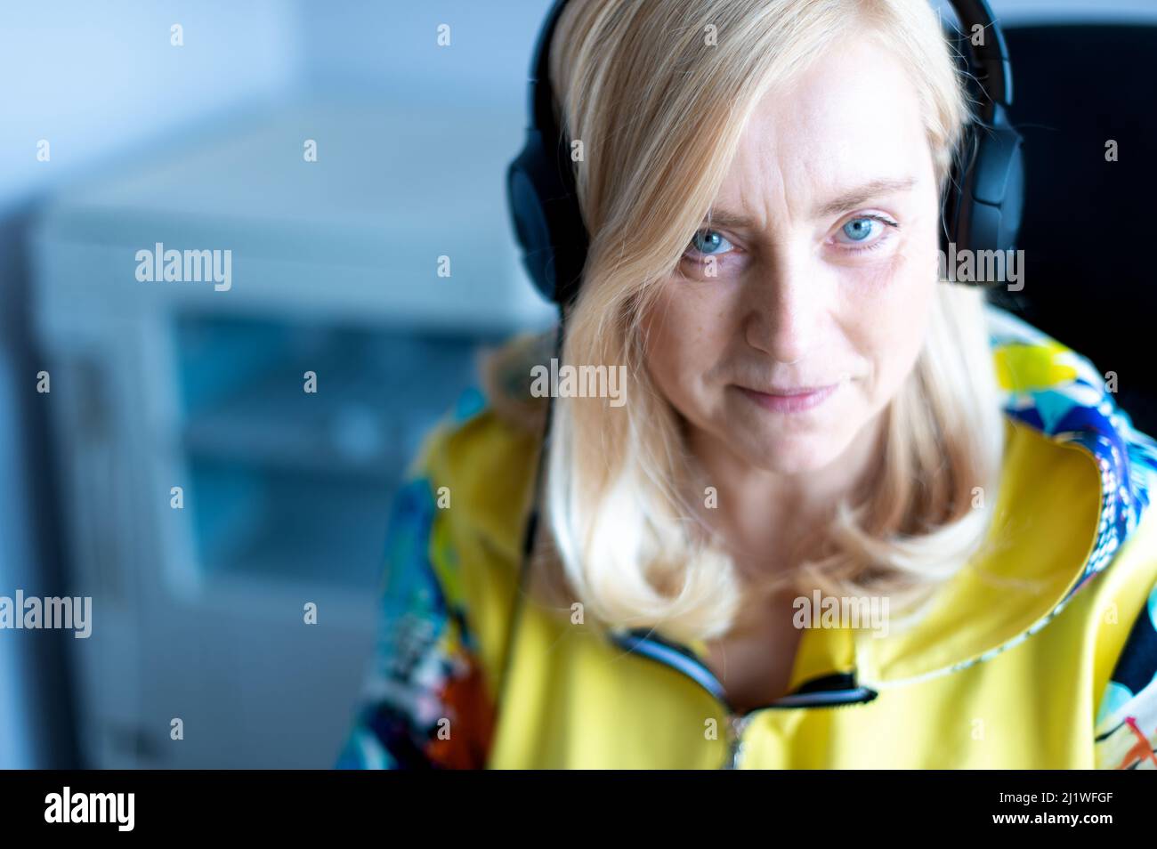 Donna da lavoro sorridente di mezza età con cuffie che guardano la fotocamera mentre si siede in ufficio Foto Stock
