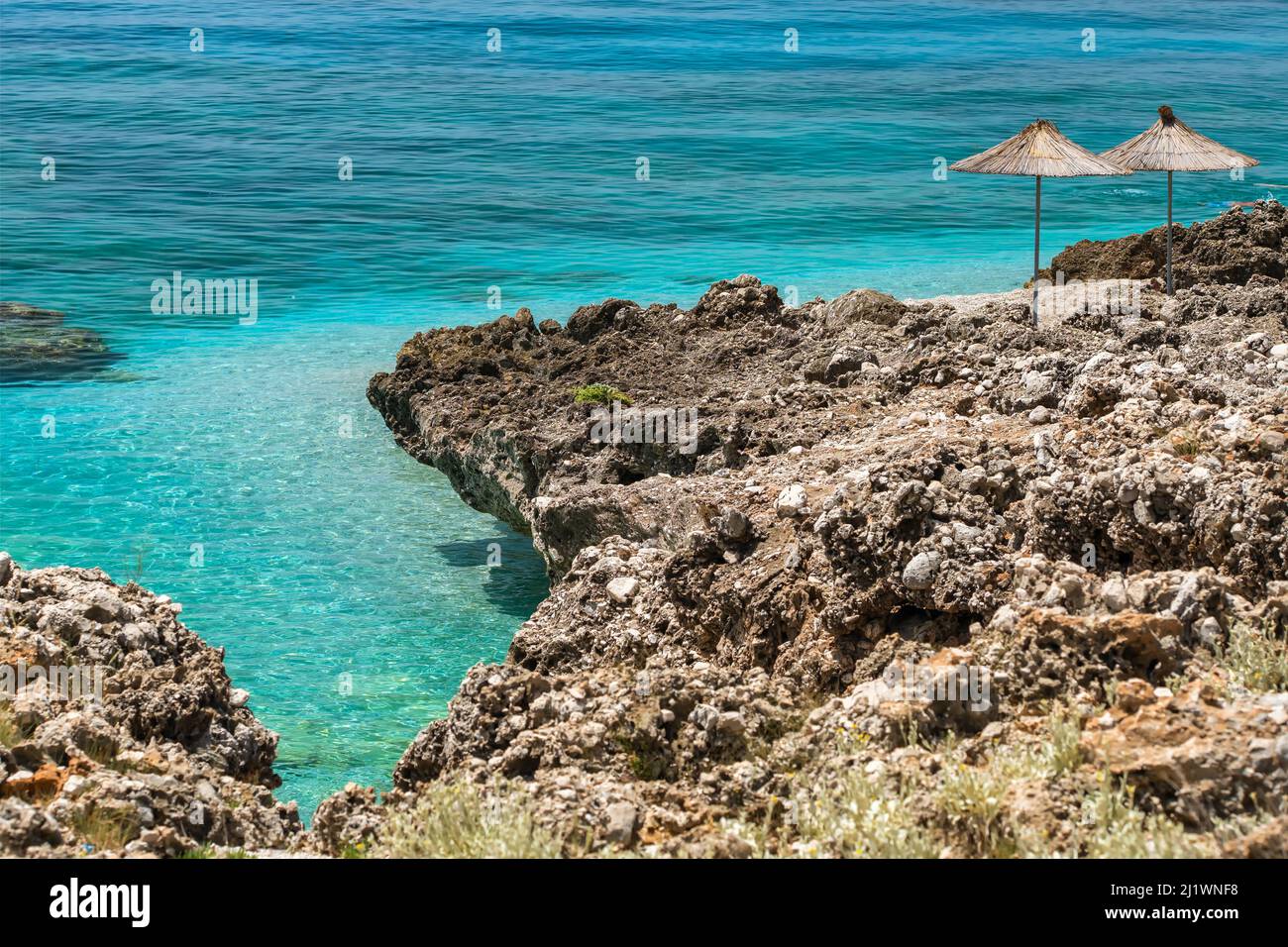 Bella spiaggia rocciosa vuota e selvaggia con ombrelloni e bella acqua di mare calma Foto Stock