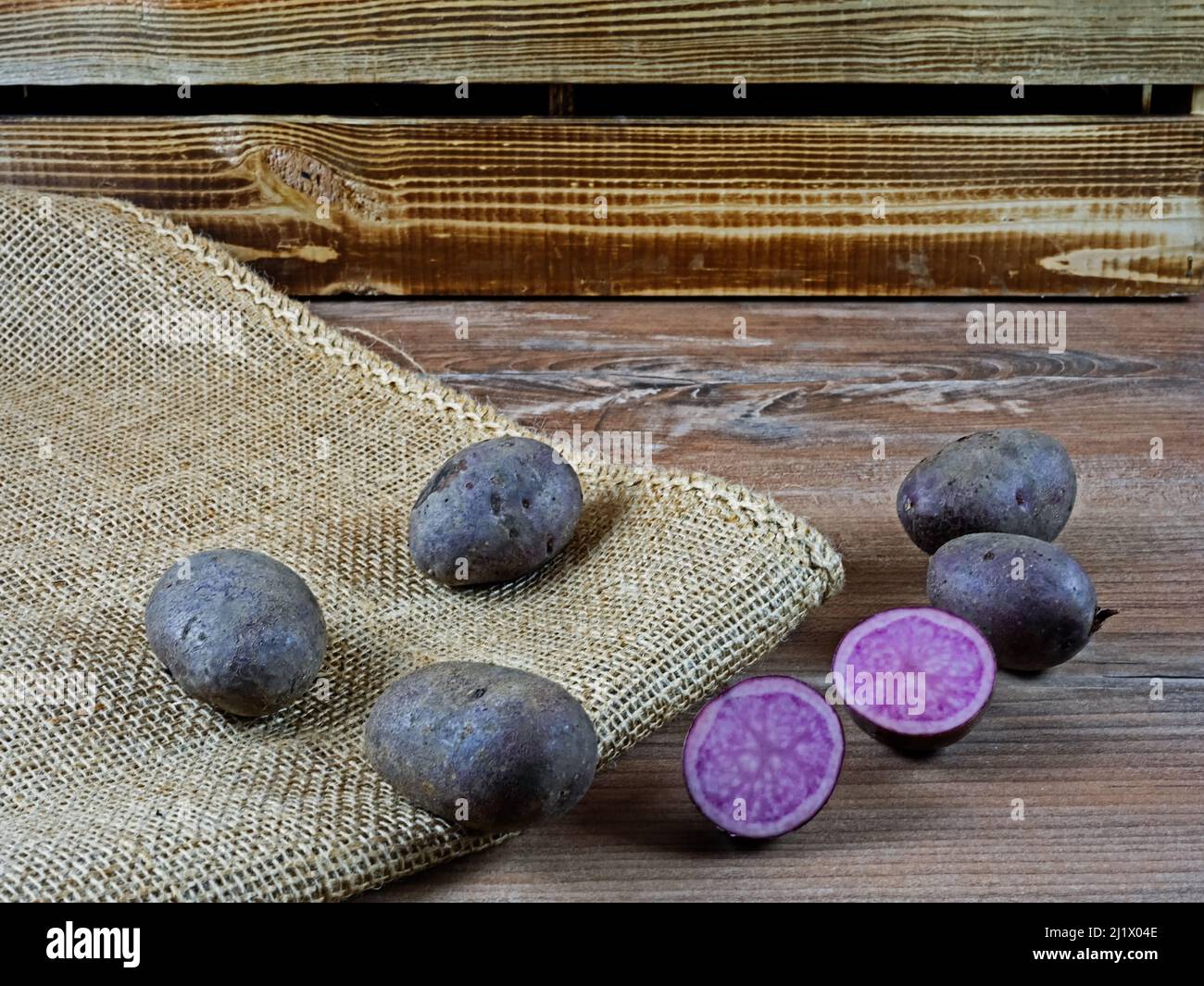 Diverse patate di viola Violetta su legno e burlap di fronte a una scatola di legno, un taglio di patate Foto Stock