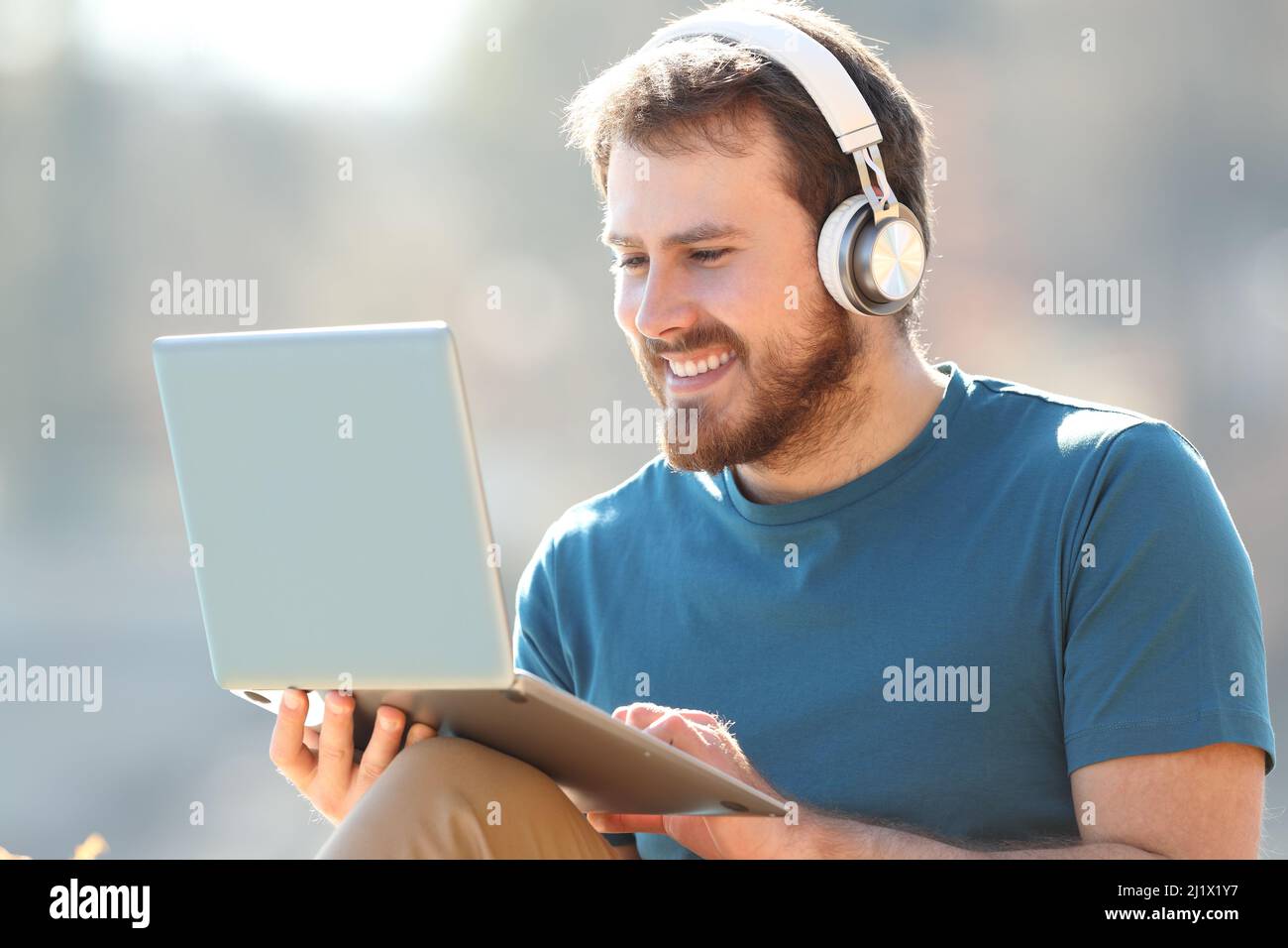 Uomo felice che indossa le cuffie wireless utilizzando un computer portatile all'aperto Foto Stock