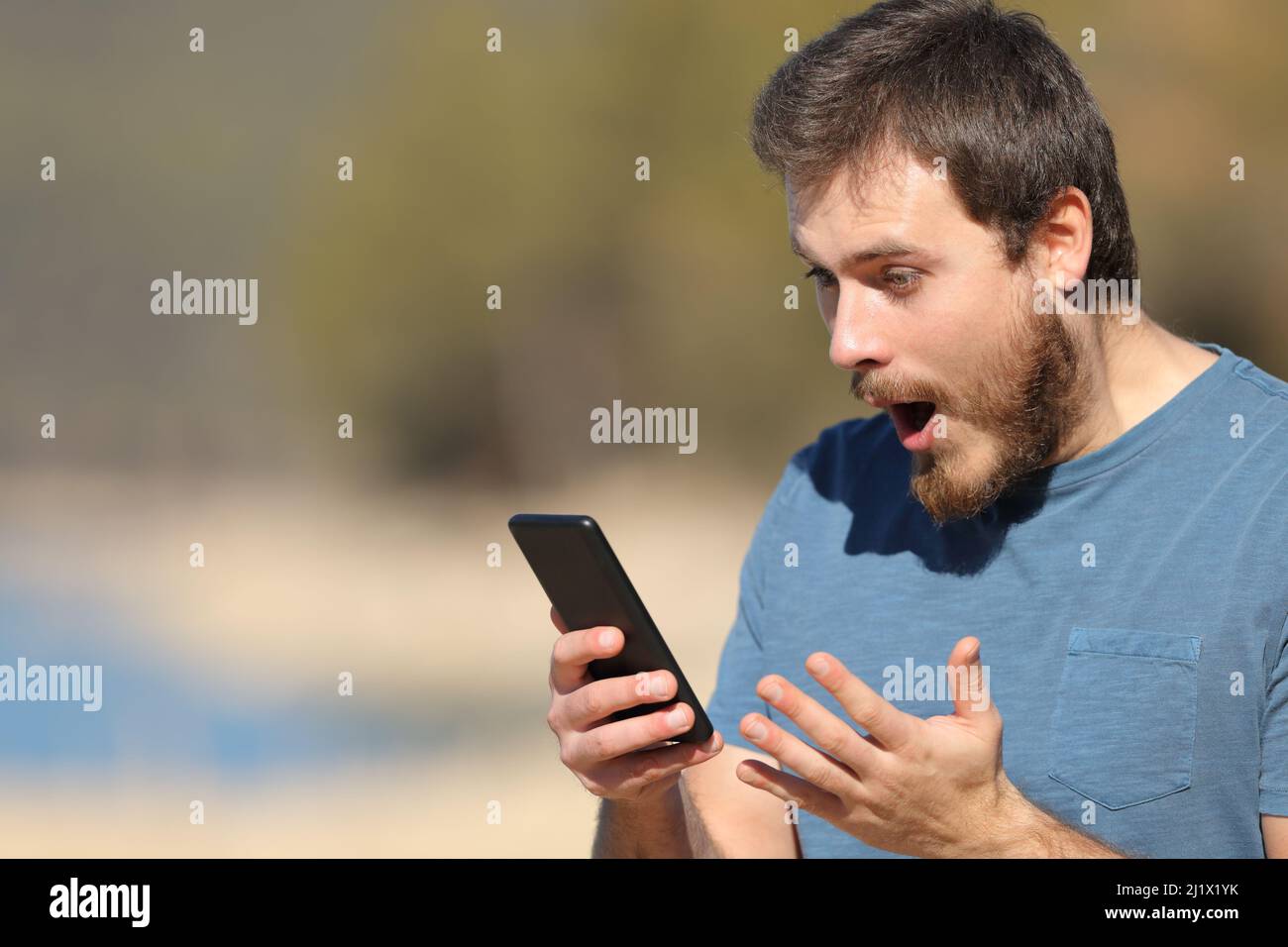 Uomo scioccato che controlla i contenuti online dello smartphone in natura Foto Stock