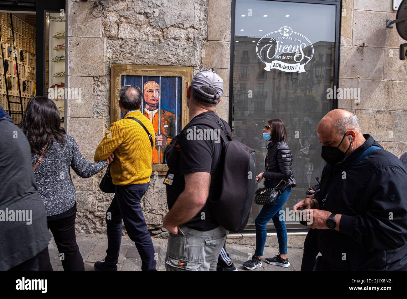 Barcellona, Spagna. 28th Mar 2022. La gente guarda avanti mentre si cammina davanti a un ritratto di Vladimir Putin dietro i bar. Vladimir Putin Behind Bars è rappresentato nel nuovo collage grafico pubblico in Plaza de Sant Jaume dall'artista italiano TvBoy, con sede a Barcellona. (Foto di Paco Freire/SOPA Images/Sipa USA) Credit: Sipa USA/Alamy Live News Foto Stock