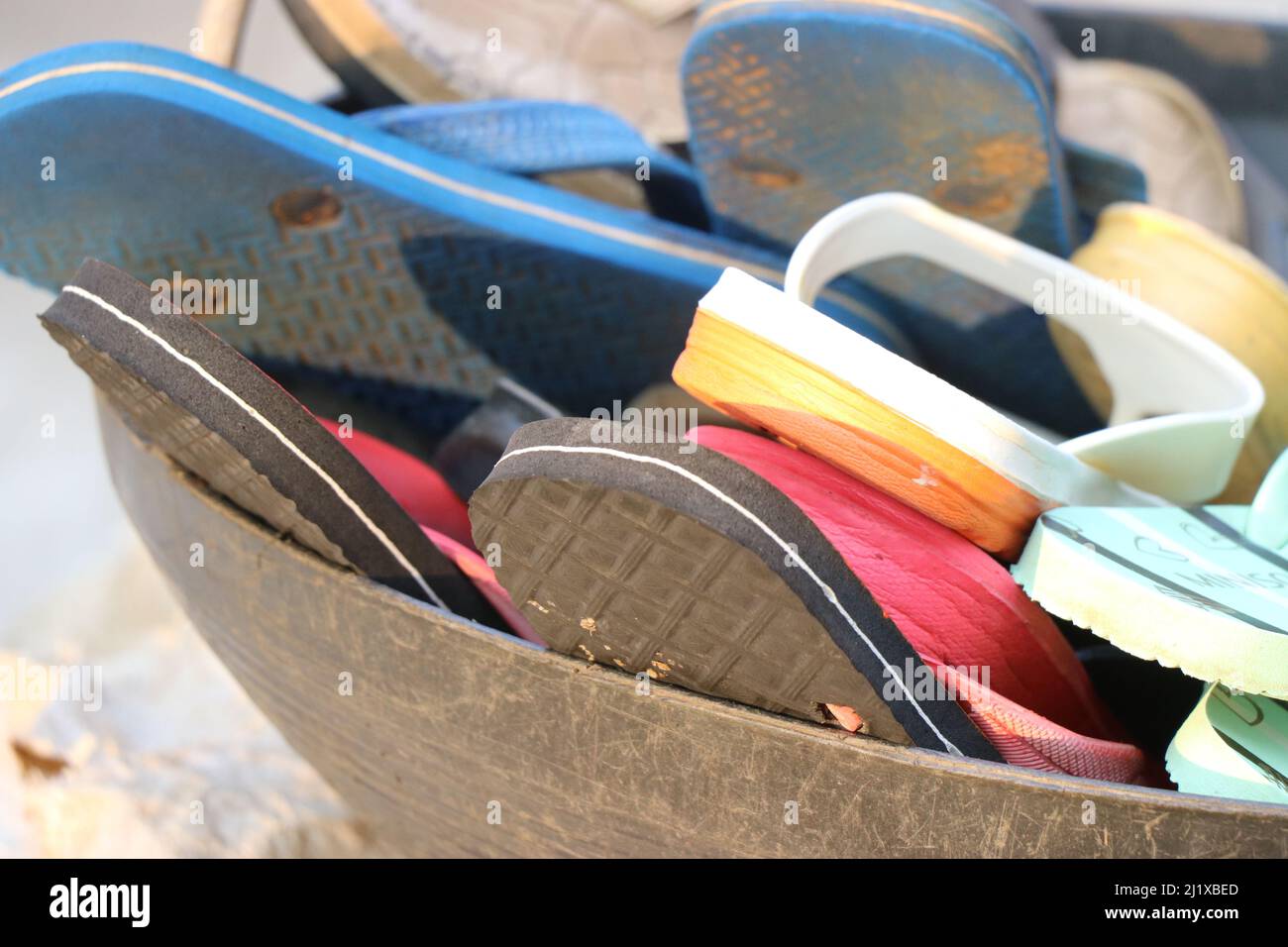 Gruppo di calzature usate poste in un cestino, flipflop colorato in un cestino Foto Stock