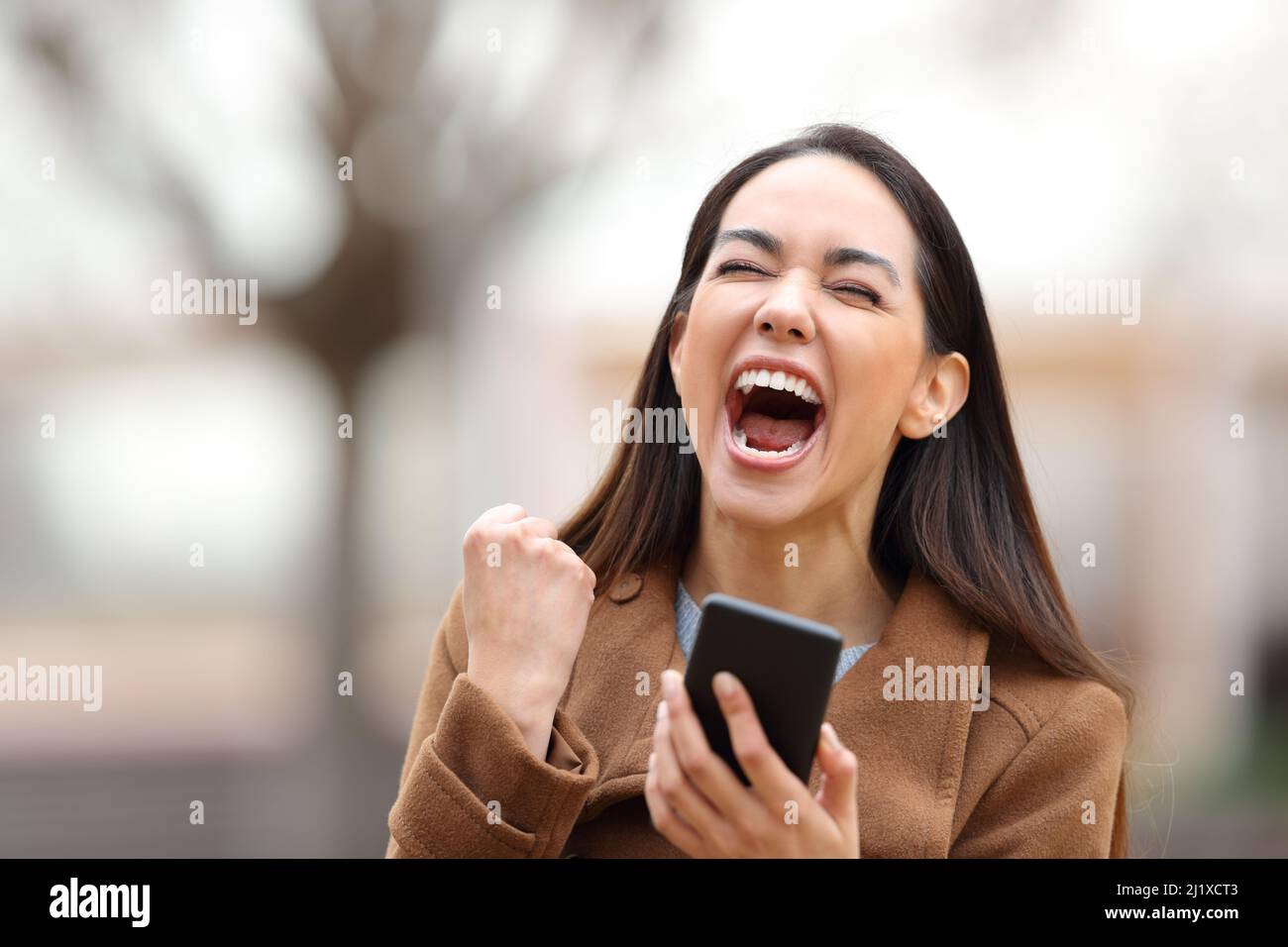 Donna eccitata che tiene il telefono cellulare celebrare le buone notizie in piedi in un parco Foto Stock