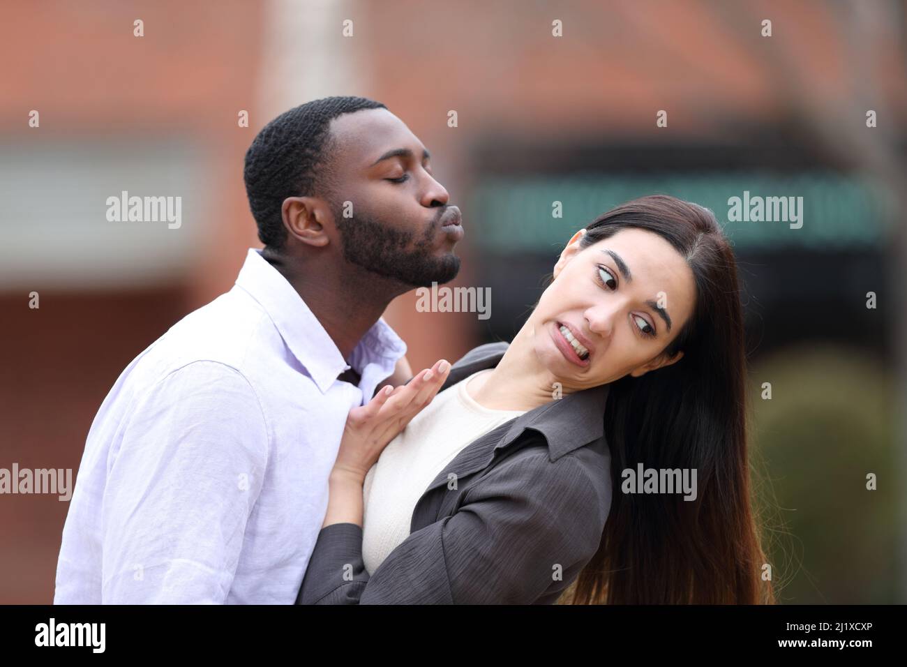 Uomo con pelle nera cercando di baciare una donna caucasica che lo allontana per strada Foto Stock