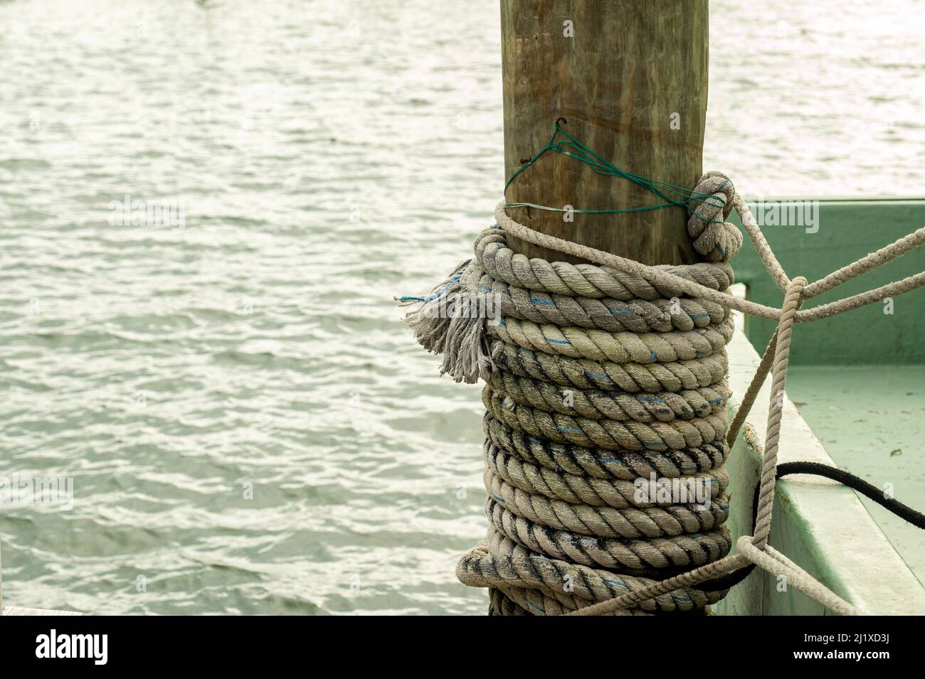 Corda nautica legata ad un palo di legno su un molo, con acqua sullo sfondo. Foto Stock
