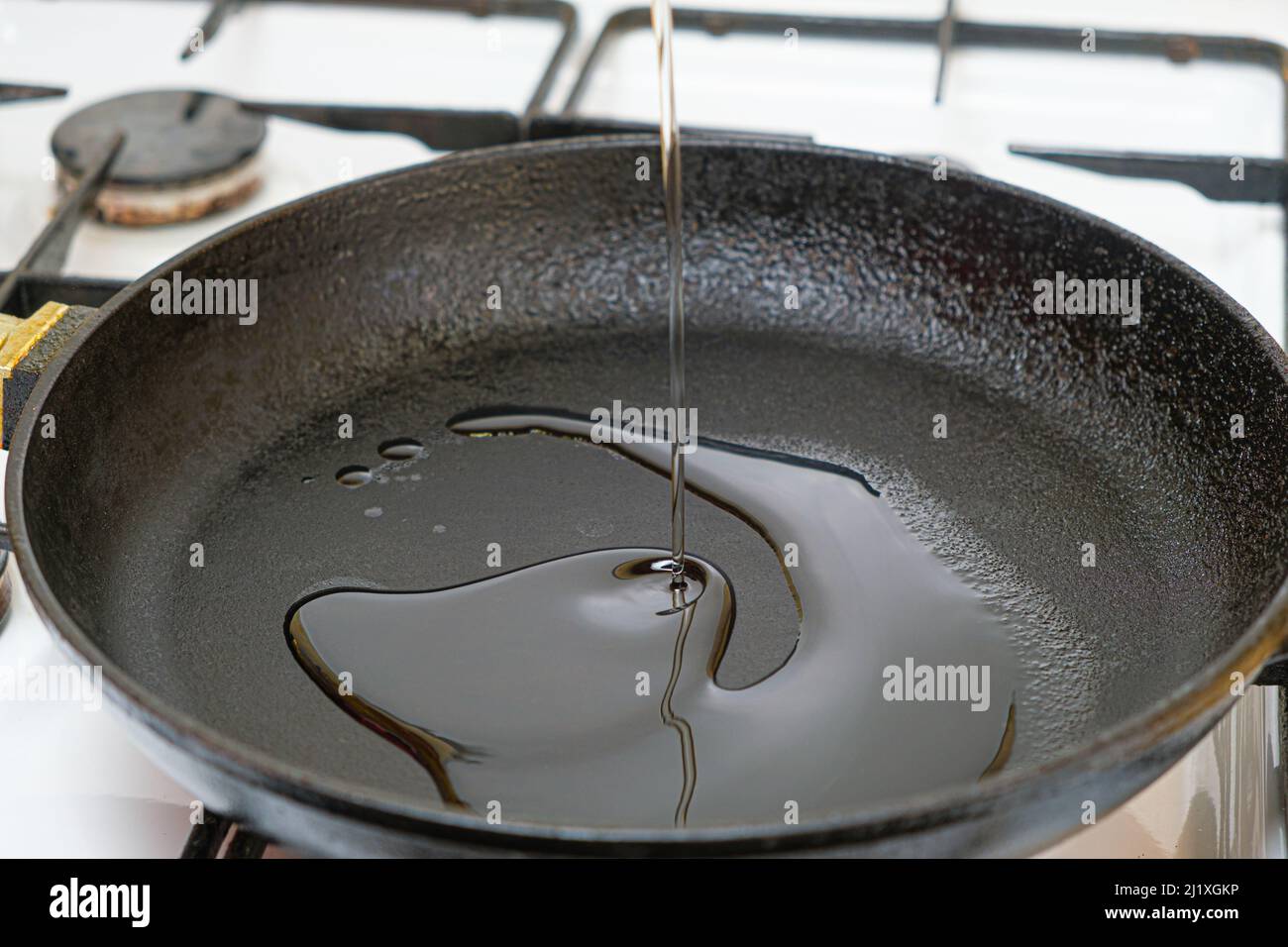 Il processo di versare l'olio vegetale in una padella riscaldata in ghisa. Foto Stock