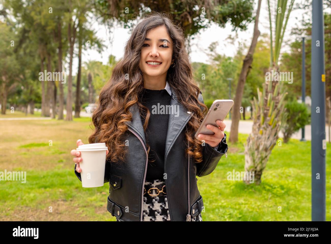 Sicura felice bella giovane donna di affari guardando la macchina fotografica con tazza di caffè e telefono. È molto felice. Positiva bella donna sorridente a cam Foto Stock