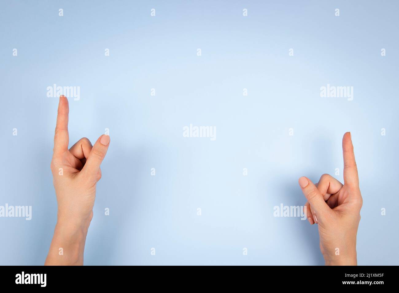 Le mani della donna puntano verso l'alto con le dita dell'indice a qualcosa di virtuale e invisibile, copia lo spazio su sfondo azzurro chiaro Foto Stock