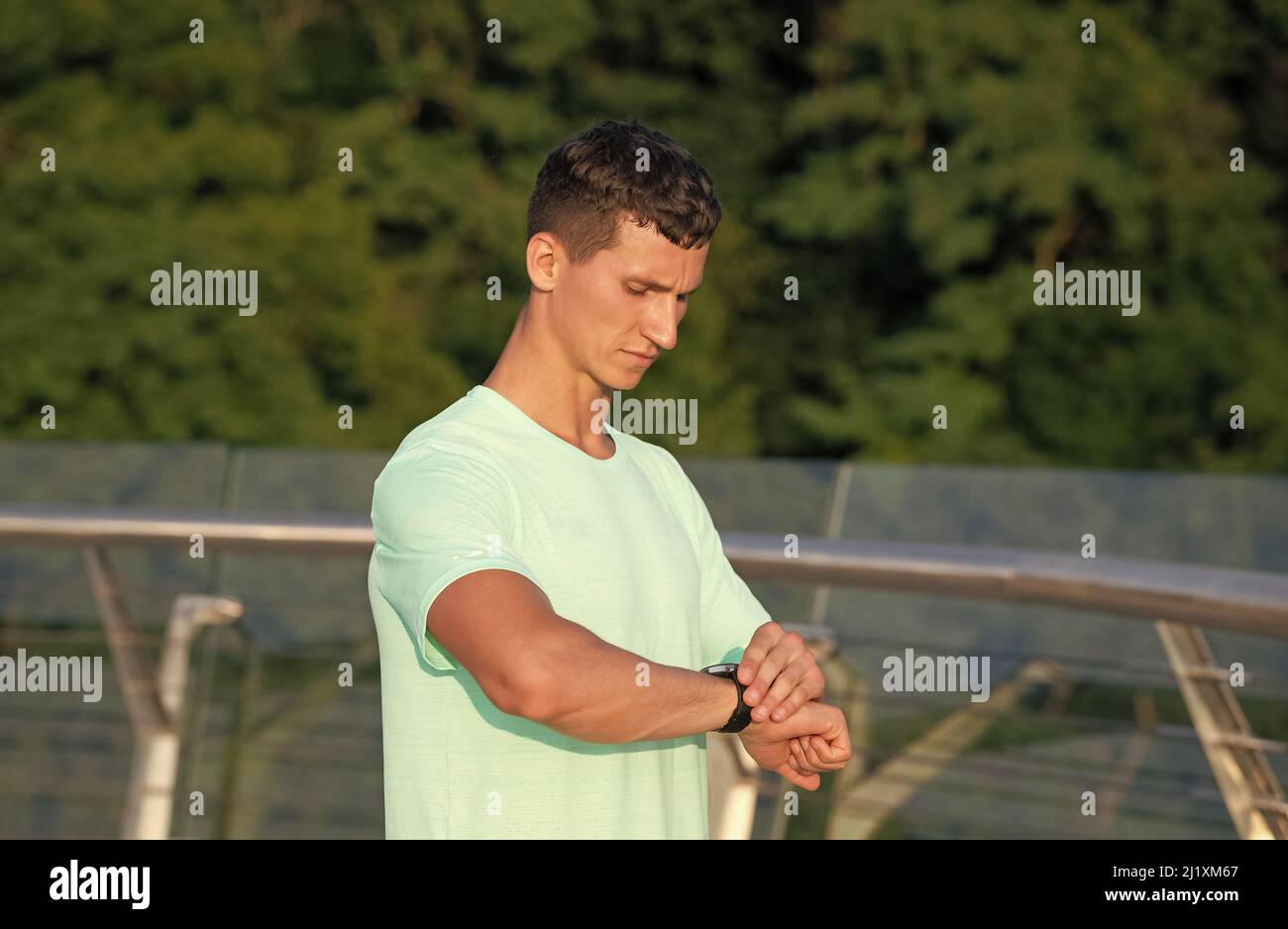L'uomo atletico controlla il tempo sull'orologio da polso durante l'allenamento all'aperto, i tempi sportivi Foto Stock