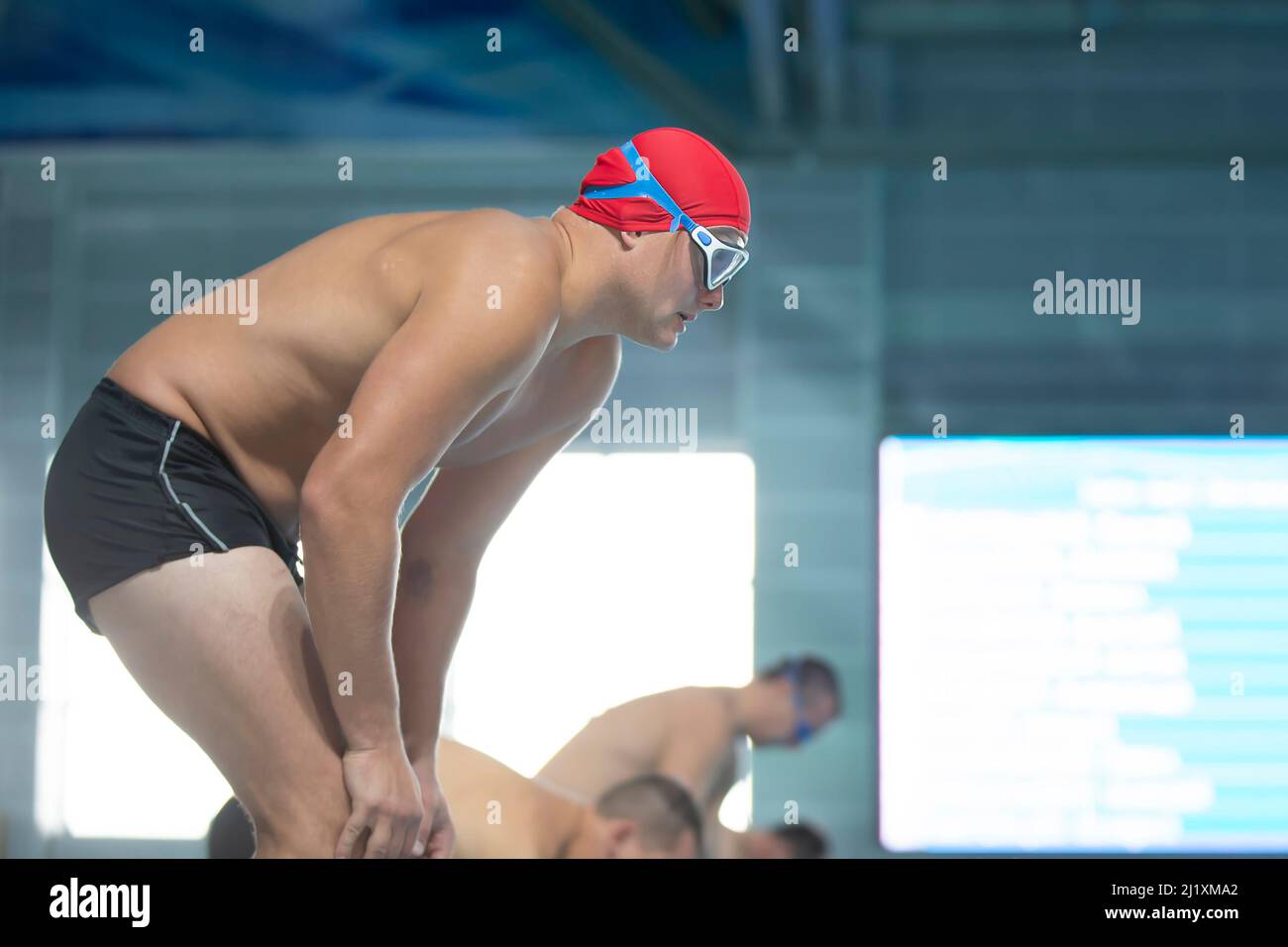 Un nuotatore maschile in una cuffia da nuoto e occhiali sullo sfondo della piscina. Foto Stock