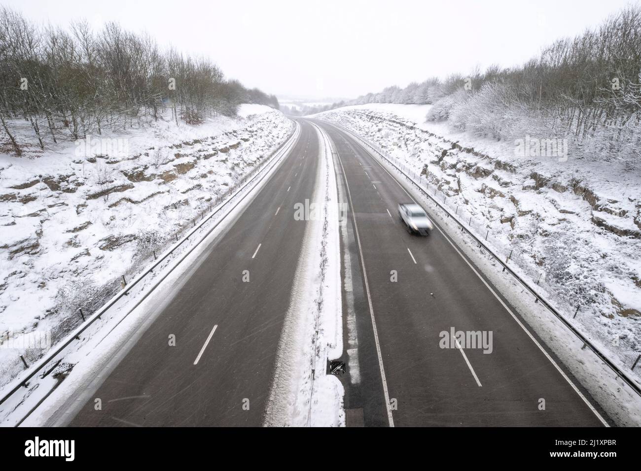 Una vista della A419 / A417 by pass con veicoli che viaggiano molto lentamente nella pericolosa condizioni stradali, nella foto dopo un pesante nevicata invernale la strada che teste attraverso il cuore di Cotswolds nel Regno Unito è a malapena praticabile in questi unusally cattive condizioni per viaggiare. Foto Stock