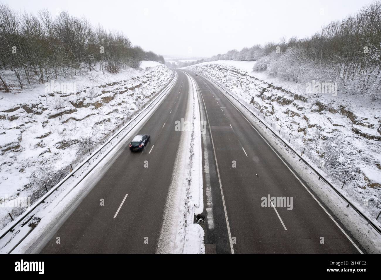 Una vista della A419 / A417 by pass con veicoli che viaggiano molto lentamente nella pericolosa condizioni stradali, nella foto dopo un pesante nevicata invernale la strada che teste attraverso il cuore di Cotswolds nel Regno Unito è a malapena praticabile in questi unusally cattive condizioni per viaggiare. Foto Stock