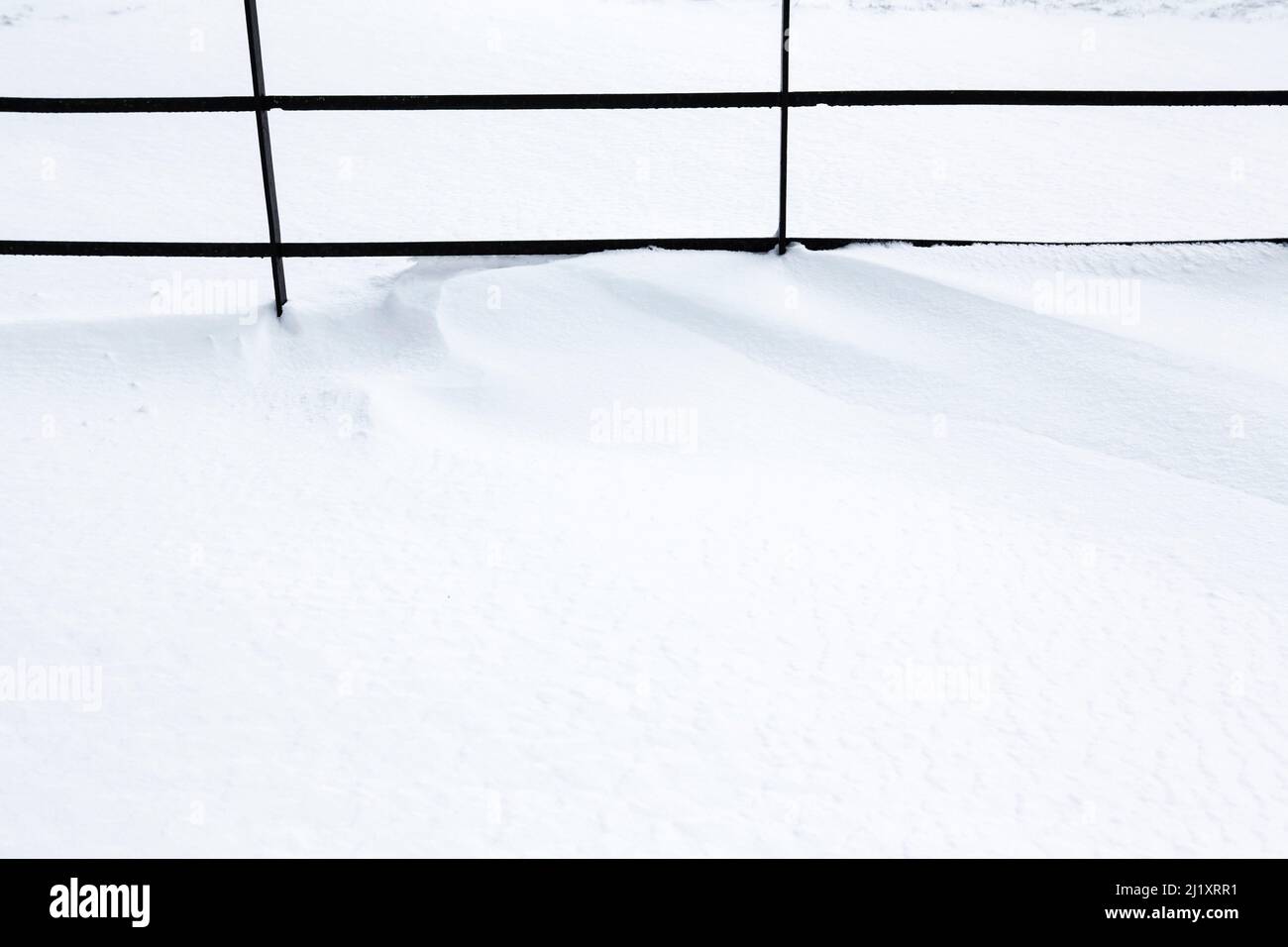 Una recinzione metallica parzialmente sepolta sotto tumuli di neve che sgocciolano. Foto Stock