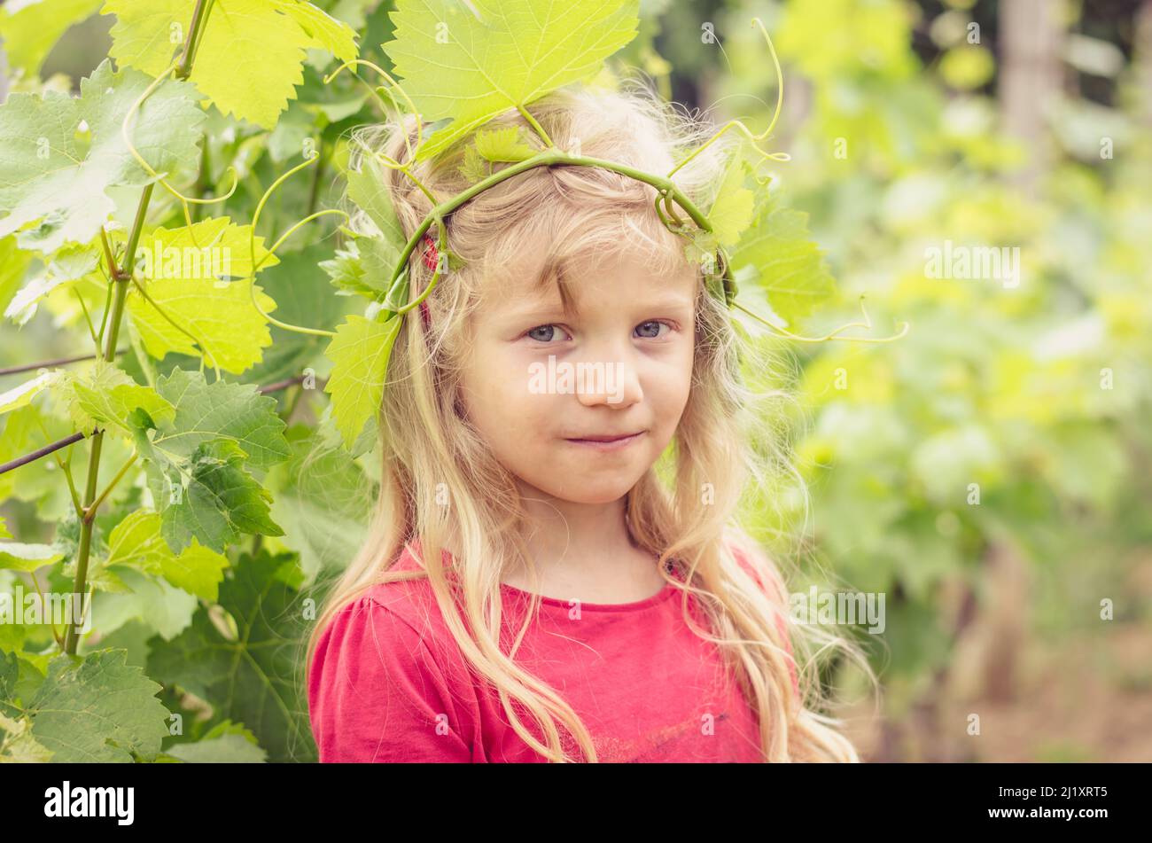 bella ragazza bionda piccola con foglie di vigneto intorno alla mano Foto Stock