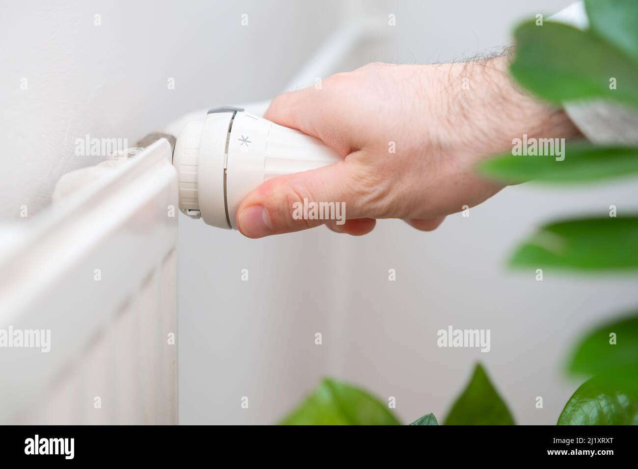 Man Hand regola la manopola di regolazione della temperatura del radiatore di riscaldamento per ridurre i costi di riscaldamento. Foto Stock