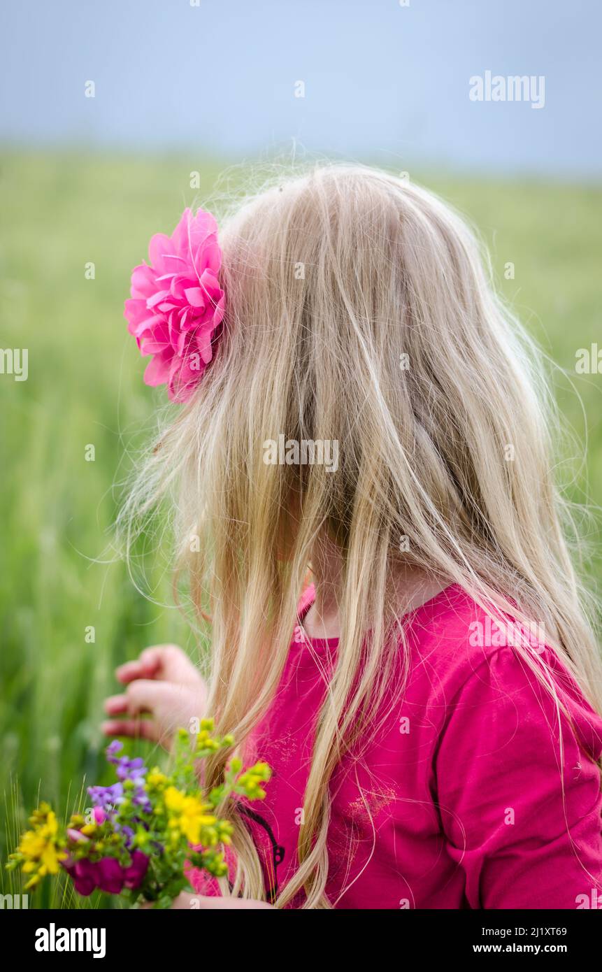 ragazza con capelli biondi lunghi vista posteriore e fiori colorati in mano Foto Stock