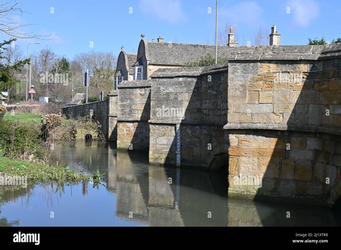 Il vecchio ponte in pietra sul fiume Windrush a Burford mostra un indicatore per i livelli di alluvione Foto Stock