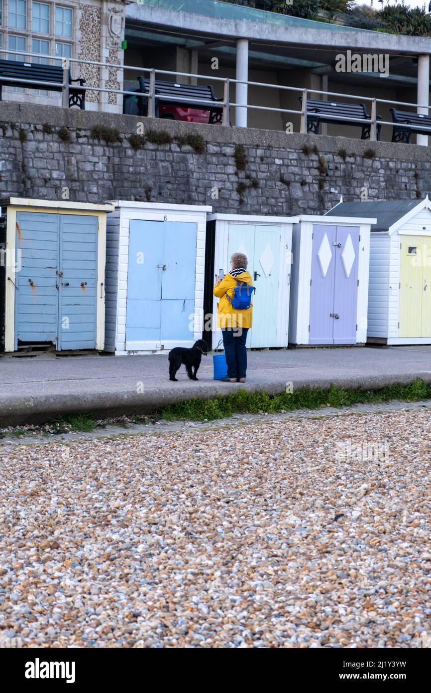 Donna che fa una foto delle capanne da banco a Lyme Regis, Regno Unito (Mar22) Foto Stock