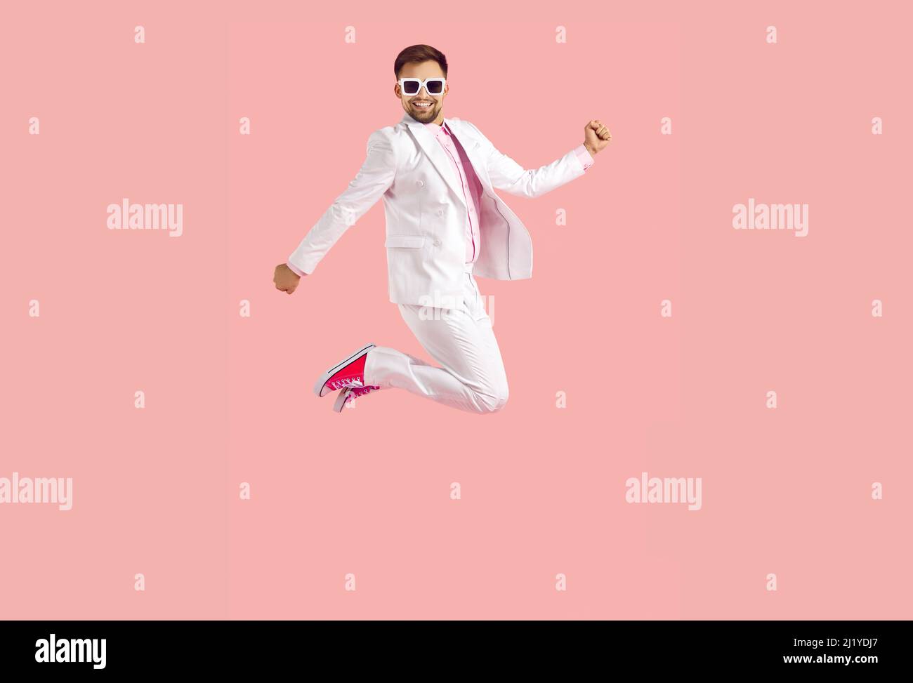 Allegro divertente giovane uomo in abito bianco salta alto isolato su sfondo rosa pastello. Foto Stock