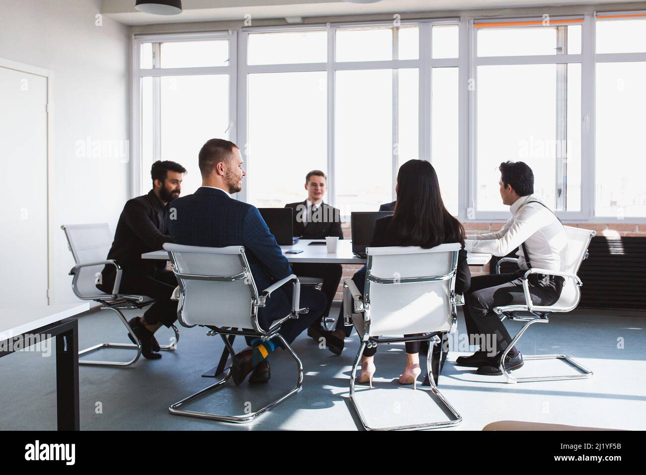 Gruppo di giovani uomini d'affari che lavorano e comunicano mentre si siedono alla scrivania dell'ufficio insieme ai colleghi seduti. Riunione d'affari Foto Stock