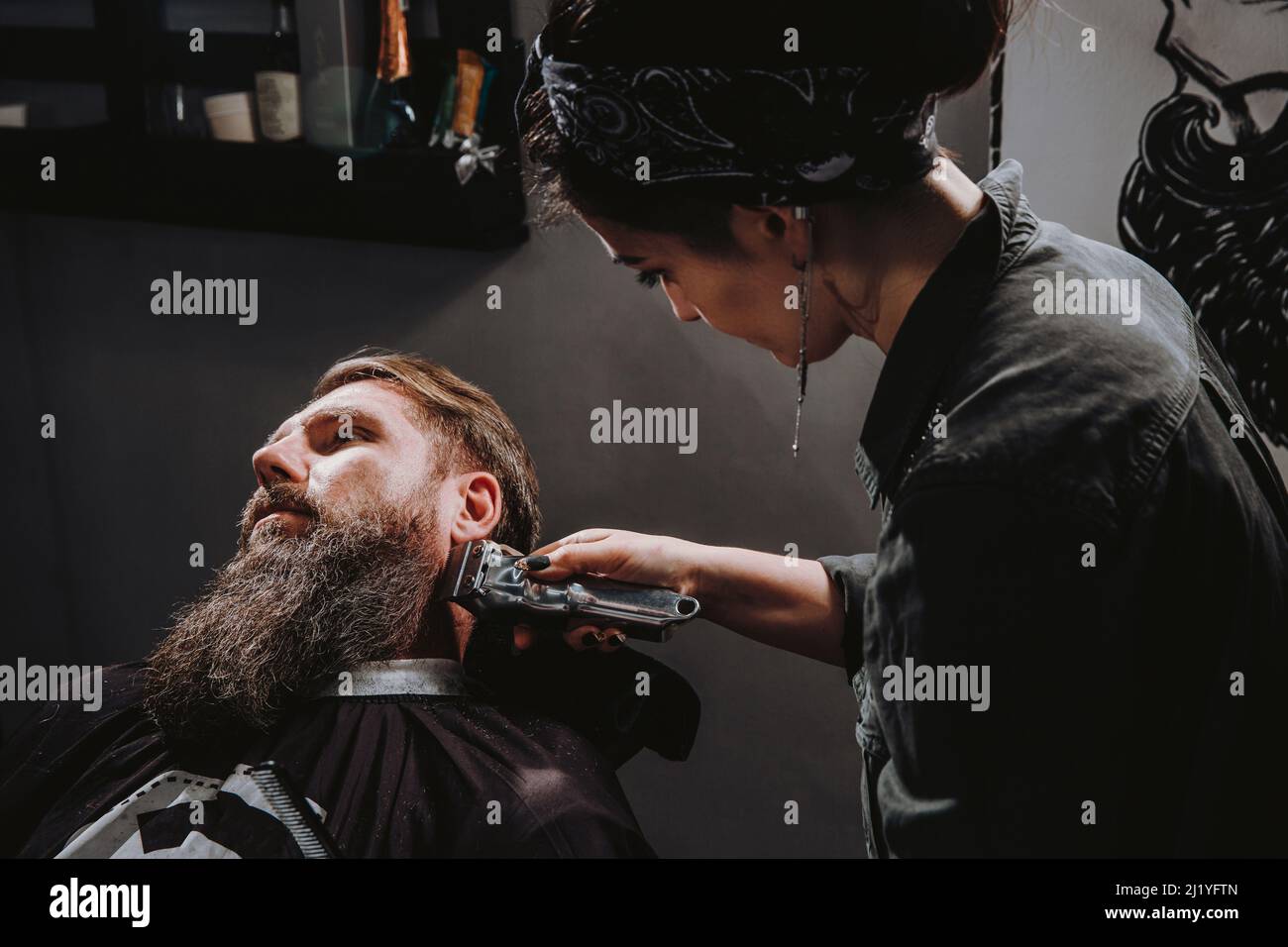 Donna professionale parrucchiere che serve il cliente con la barba folta grande da Clipper, brutale bello uomo giovane alla moda ottenere taglio di capelli alla moda, nero barbiere sala negozio Foto Stock