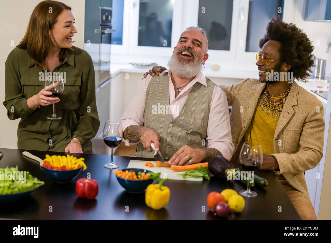 Felice gruppo di amici multigenerazionali divertirsi durante la preparazione di una cena vegetariana, bere vino rosso, concentrarsi sul hipster barbuto uomo Foto Stock