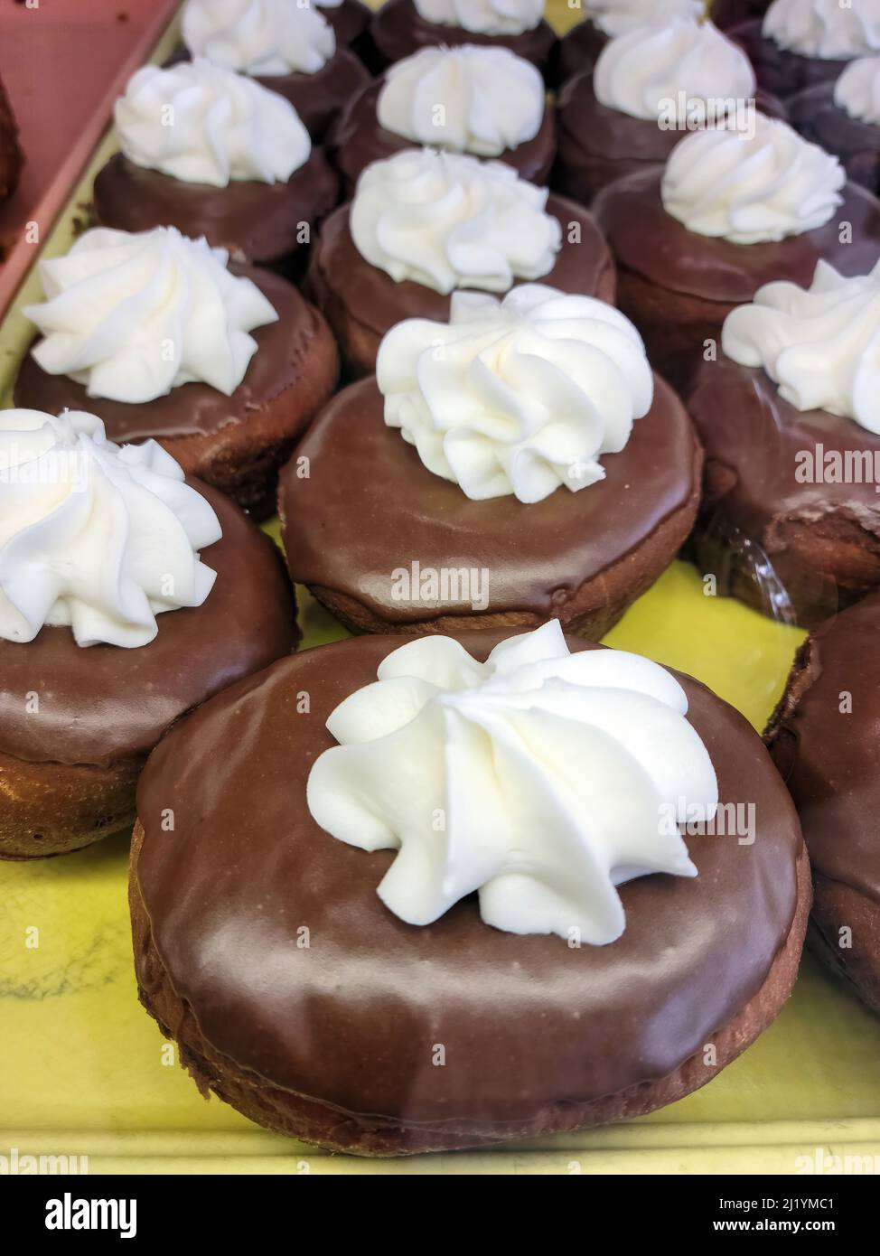 La crema bianca rotola sulle ciambelle di cioccolato su uno scaffale da forno Foto Stock