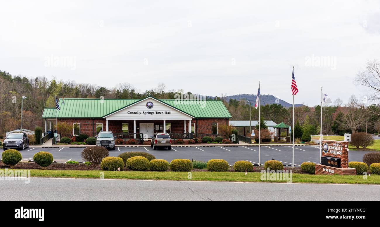 CONNELLY SPRINGS, NC, USA-24 MARZO 2022: Edificio del municipio, parcheggio, bandiere, pali, e cartello monumento a lato strada. Giorno di primavera. Foto Stock